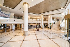A spacious lobby with a high ceiling, large columns, a central staircase, and a reception area.