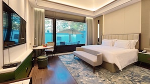 Hotelkamer met een groot bed, een klein tafeltje met een bloevas, een bankje, een raam met gordijnen en uitzicht op de omgeving.