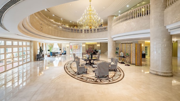 Een ruime lobby met een weelderige kroonluchter, een centraal gelegen zithoek en een balkon op de tweede verdieping.