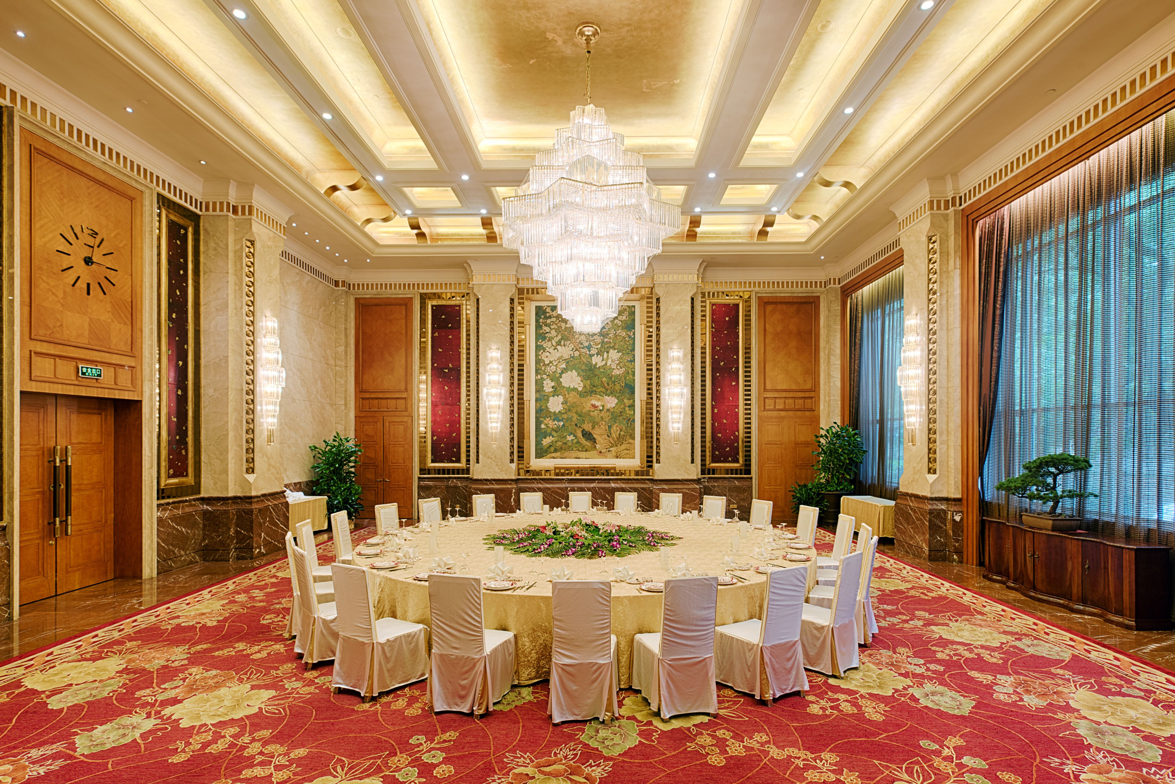 A large conference room with a round table, white chairs, and a chandelier.
