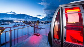 A snow-covered mountain landscape with a view of a town and a building with a red-lit interior. - Hotel die Hindenburg (Saalfelden am Steinernen Meer)