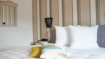 A neatly made bed with white and patterned pillows, a bedside lamp, and a nightstand with a phone.