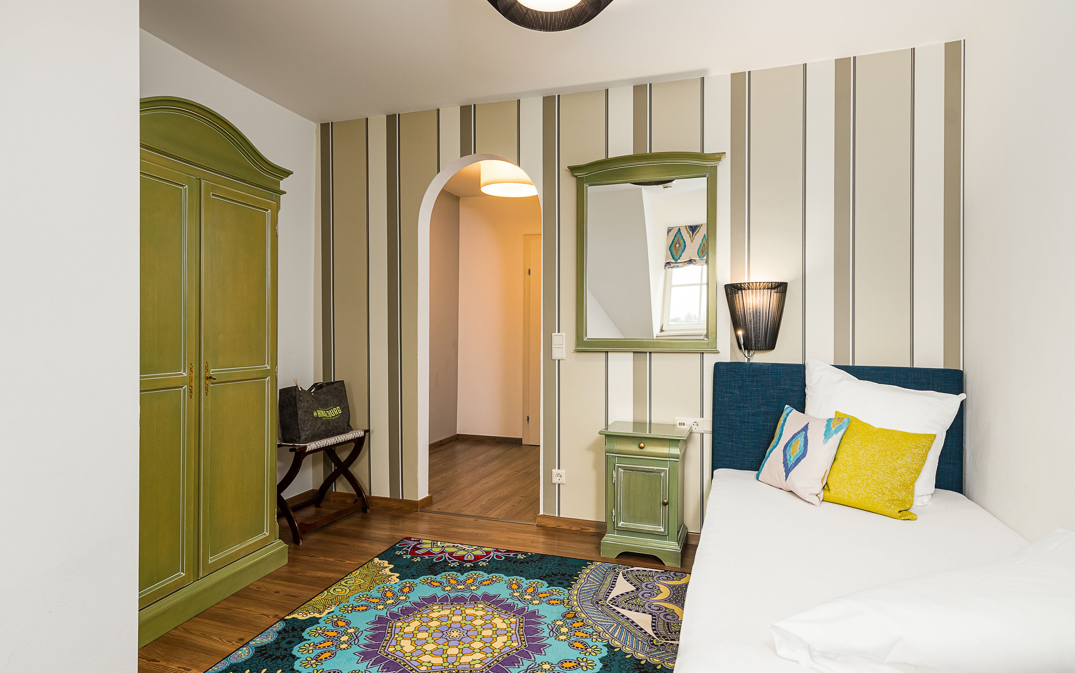 Une chambre à coucher comprenant un lit, une commode, un miroir et une porte donnant sur une autre pièce.