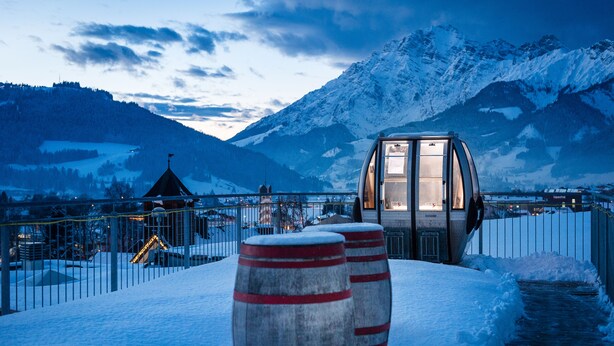A snow-covered outdoor area with a glass-enclosed structure, possibly a viewing platform or small building, and two large barrels. - Hotel die Hindenburg (Saalfelden am Steinernen Meer)