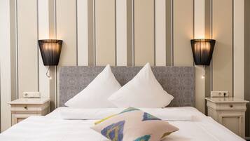 Una cama bien hecha con sábanas blancas y almohadas decorativas, cabecera gris con diseño, y dos lámparas fijadas a la pared a cada lado.