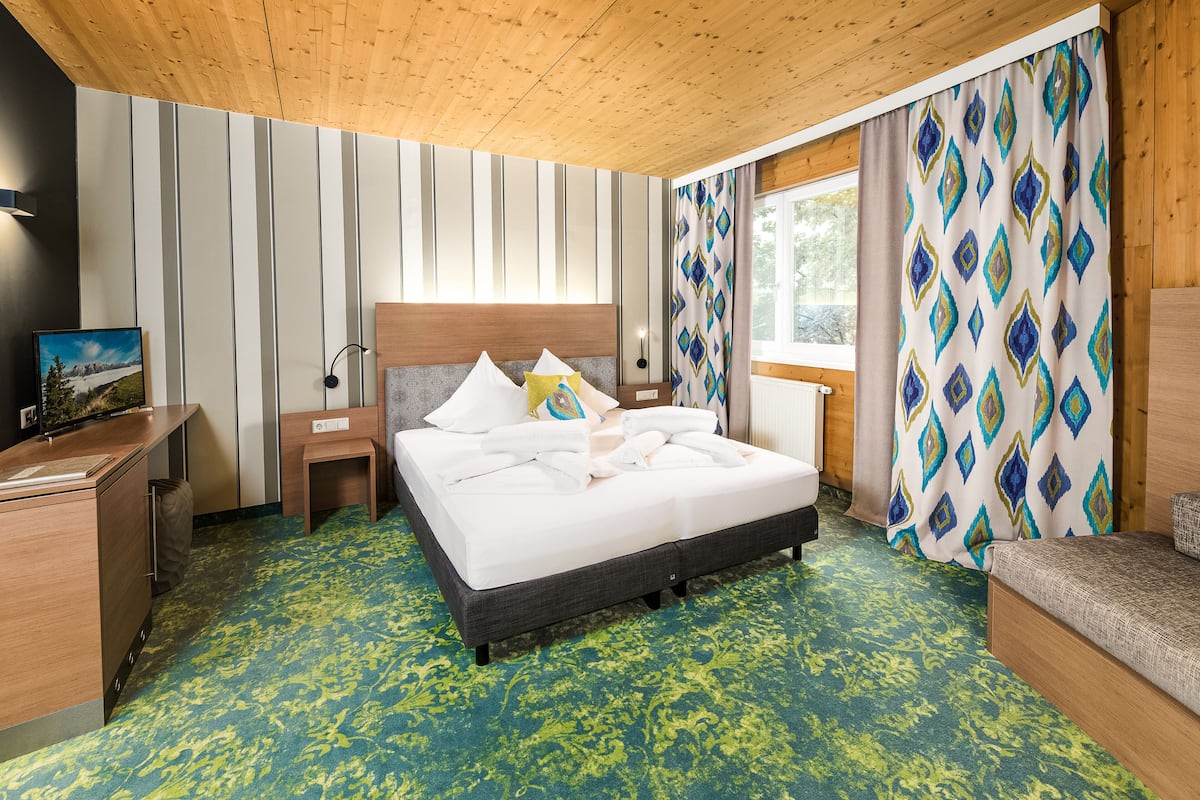 A hotel room with a bed, bedside tables, a desk, and a window with curtains.