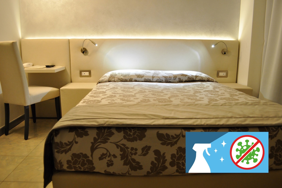 Una habitación de hotel con cama, una silla, una mesita y una mesita de noche.
