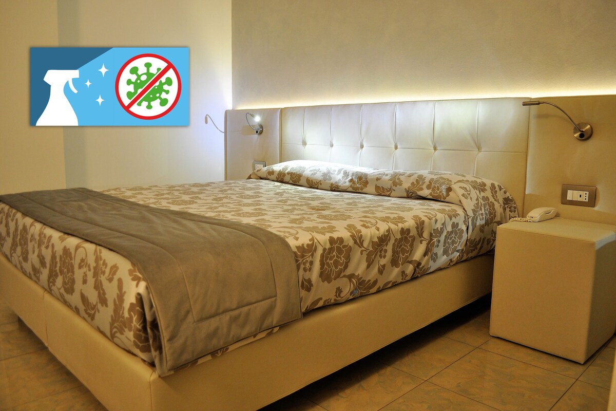 Una cama bien hecha con una colcha estampada, una mesita de noche con lámpara y una lámpara de pared.