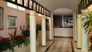 A hallway with cream-colored pillars, a checkered floor, and framed artwork on the walls. - Hotel Garibaldi (Mestre)
