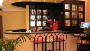 A bar area with a curved counter, multiple stools, a television screen, and a shelf with bottles. - Hotel Garibaldi (Mestre)