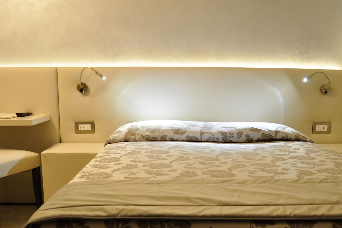 Una habitación de hotel con cama, una silla, una mesita y una mesita de noche.
