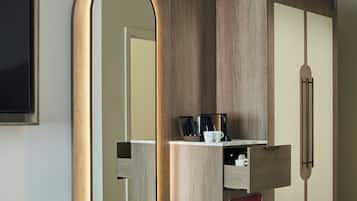 A hotel room with a large mirror, a wardrobe, and a small shelf with a coffee maker and mug.