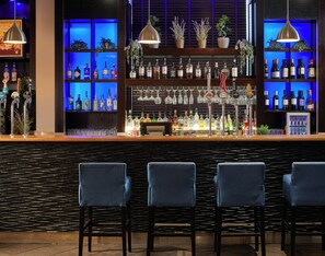 A bar area with multiple liquor bottles, glasses, and blue chairs. - Leonardo Hotel Newcastle (Newcastle-upon-Tyne)