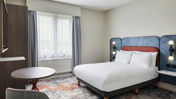 A hotel room with a bed, a round table, a chair, and a window with curtains.