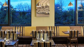 A restaurant with a view of trees and a building through large windows. There are tables and booths with striped upholstery.