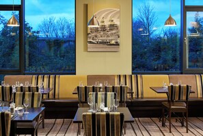 A restaurant with a view of trees and a building through large windows. There are tables and booths with striped upholstery.