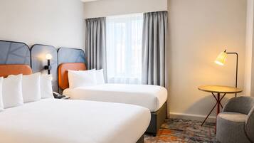 A hotel room with two beds, a desk, a chair, a lamp, and a window with curtains.