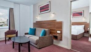 A hotel room with a sofa, a small table, a bed, and a view of the city.