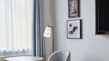 Habitación de hotel con cama, una mesa redonda, una silla, una lámpara de pie y dos cuadros en la pared.