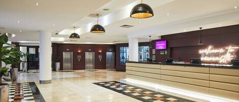 A hotel lobby with a reception desk, elevators, and a check-in counter.