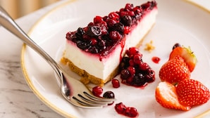 A slice of cheesecake with berries on a plate, accompanied by strawberries and a fork.