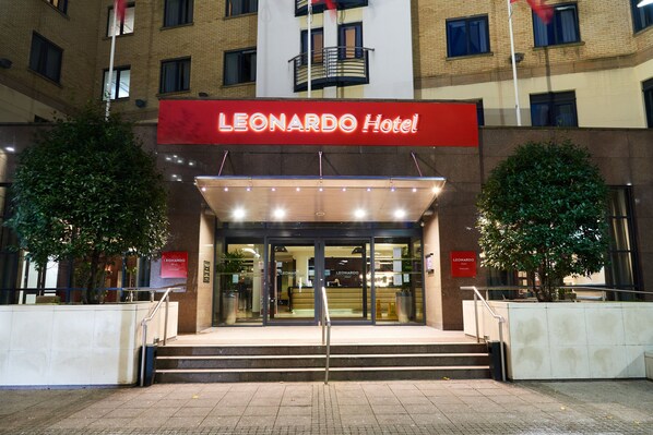 The exterior of the Leonardo Hotel with a prominent red sign, a set of stairs leading to the entrance, and two trees flanking the entrance. - Leonardo Hotel Newcastle (Newcastle-upon-Tyne)