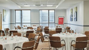 Un salón de conferencias con varias mesas, sillas y una pantalla de proyector.
