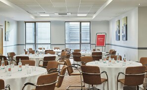 Une salle de conférence équipée de plusieurs tables, de chaises et d’un écran de projection.