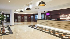 A hotel lobby with a reception desk, elevators, and a check-in counter.