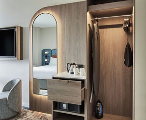Una habitación de hotel moderna con un tocador de madera, un espejo, una cama, una silla y un televisor.