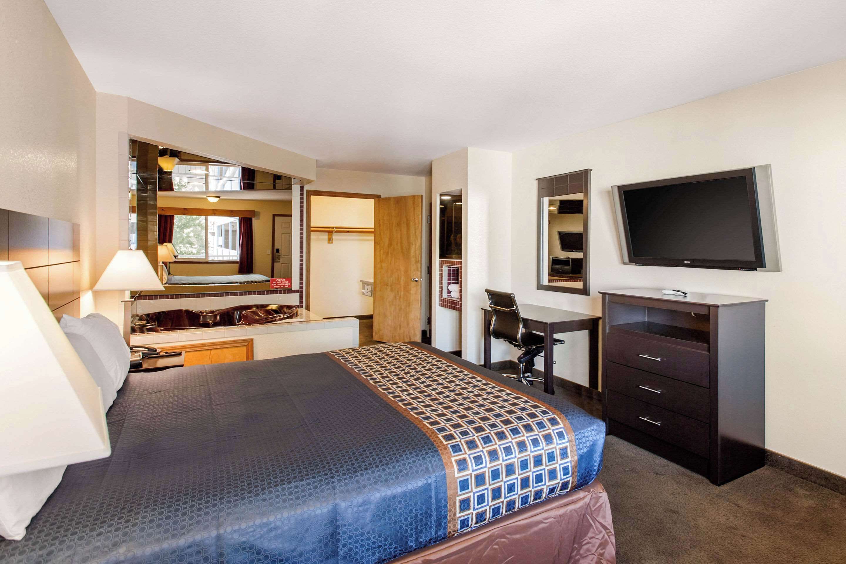 A hotel room with a bed, desk, chair, TV, and a small kitchenette area.