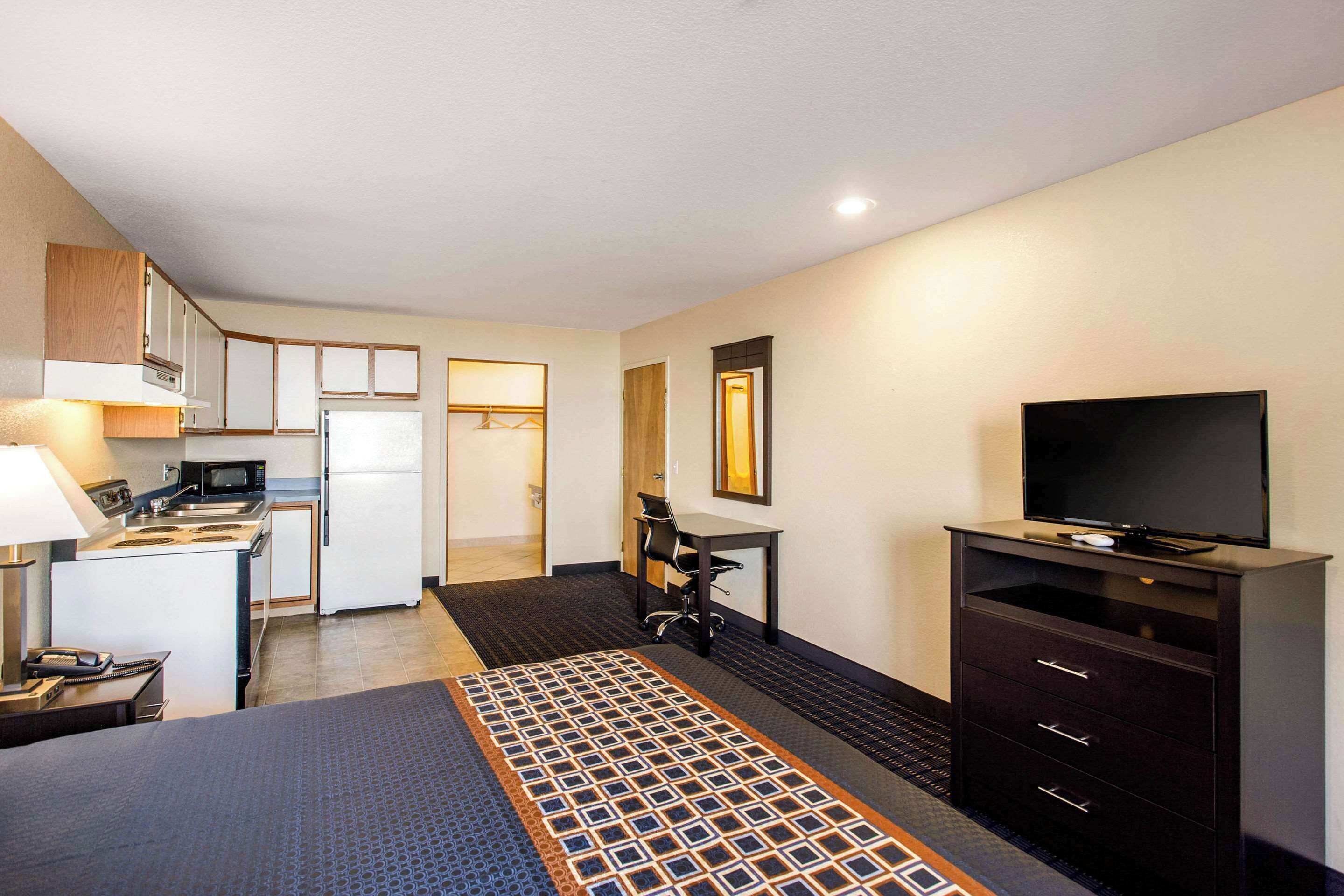 Una habitación de hotel con cama, escritorio, televisor, kitchenette y baño.