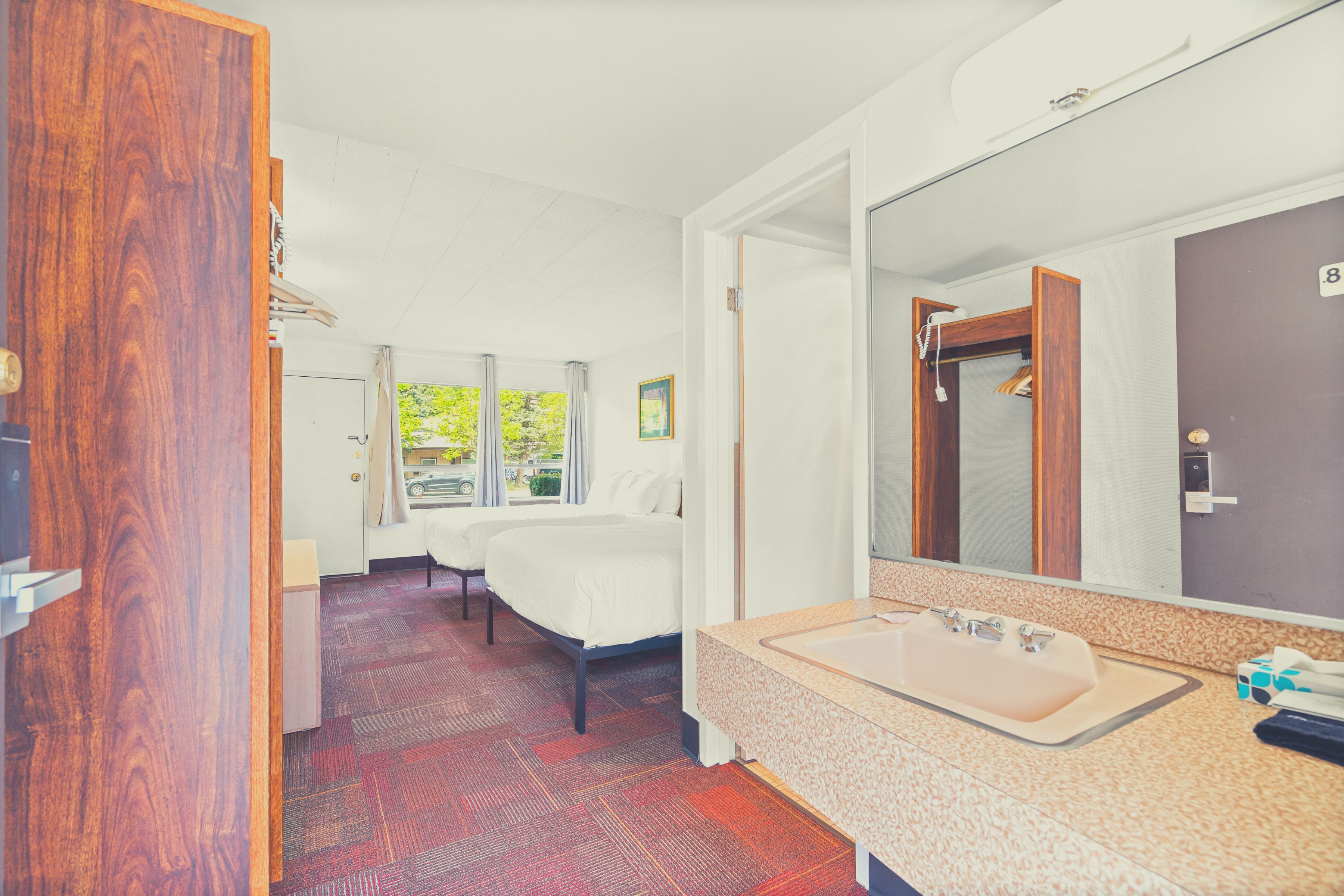 Habitación de hotel con una cama grande, una cama doble, un baño con lavamanos y espejo, y vistas a zonas verdes.