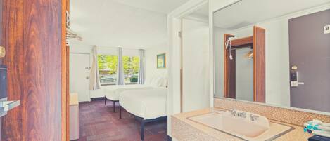 Hotelkamer met een groot bed, een tweepersoonsbed, een badkamer met wastafel en spiegel, en uitzicht op groen.