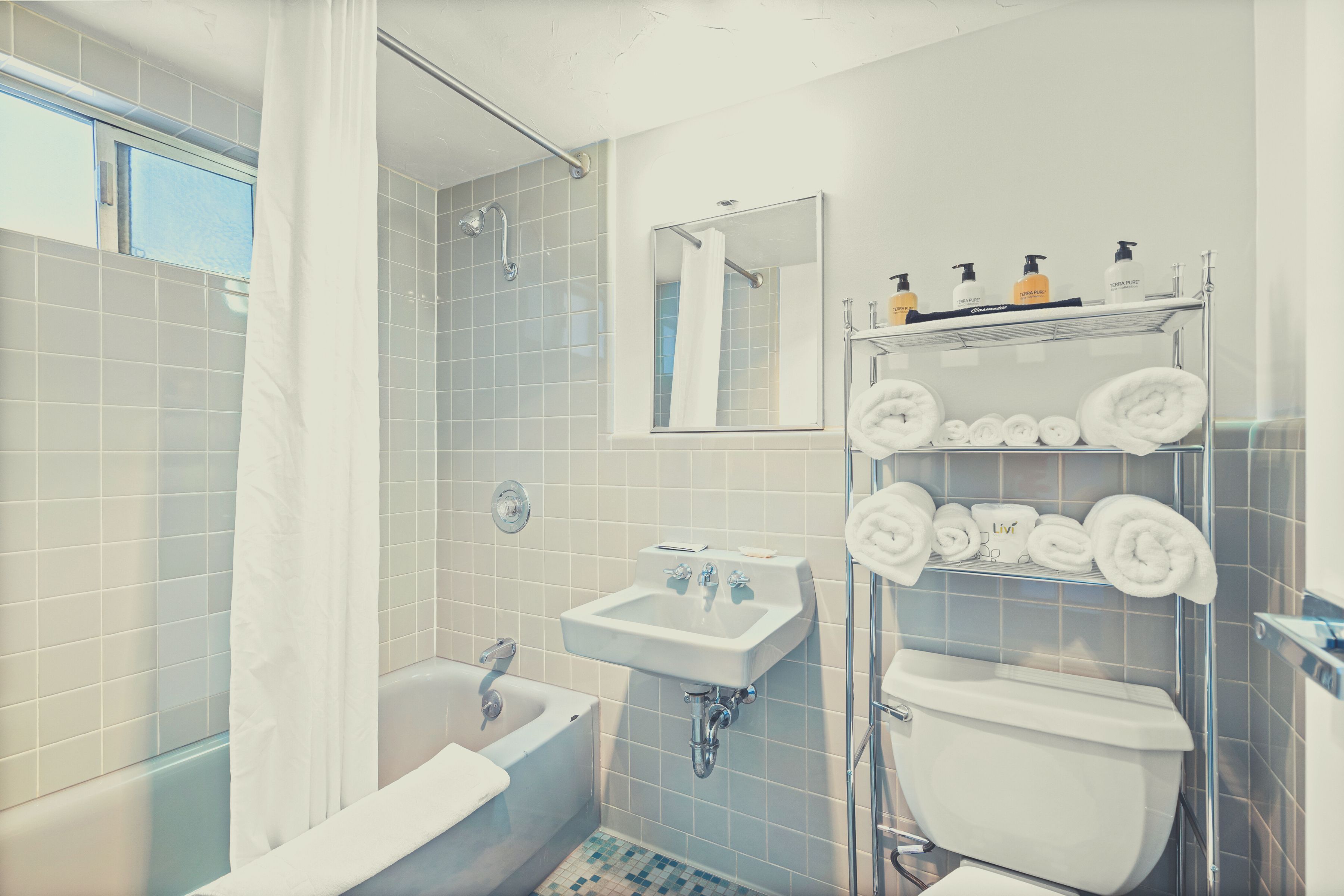 A bathroom with a bathtub, sink, and toilet, with towels and toiletries on shelves.