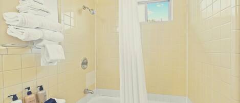 A bathroom with yellow tiled walls, a white bathtub, a shower area, and a window with a view.