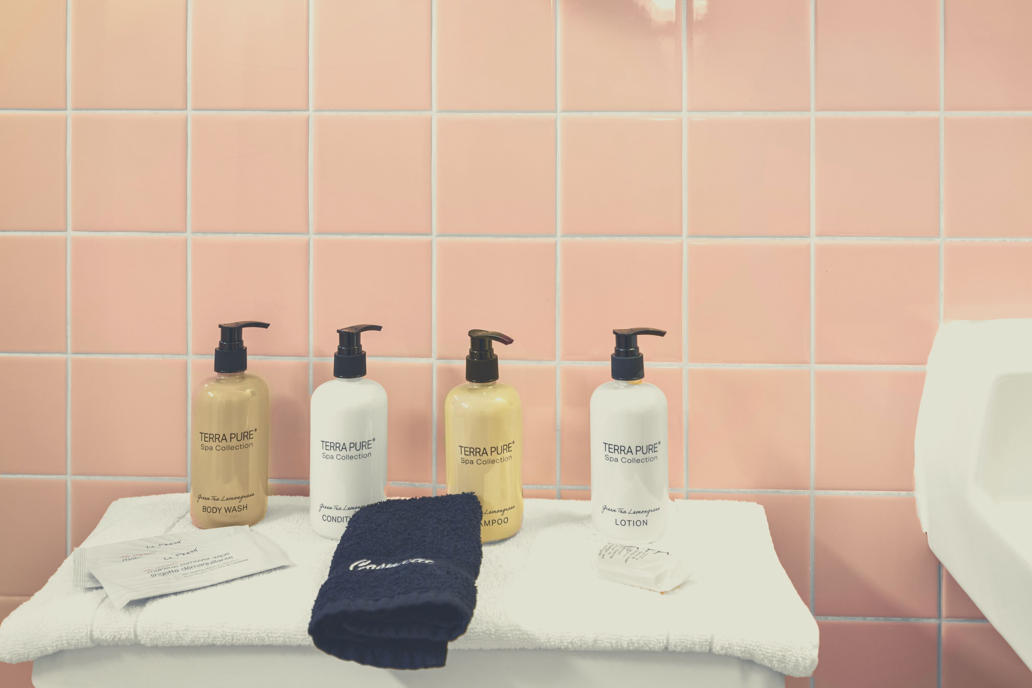 Un baño con un lavabo blanco, un espejo y cuatro botellas de la colección Terra Pure Spa sobre una toalla.