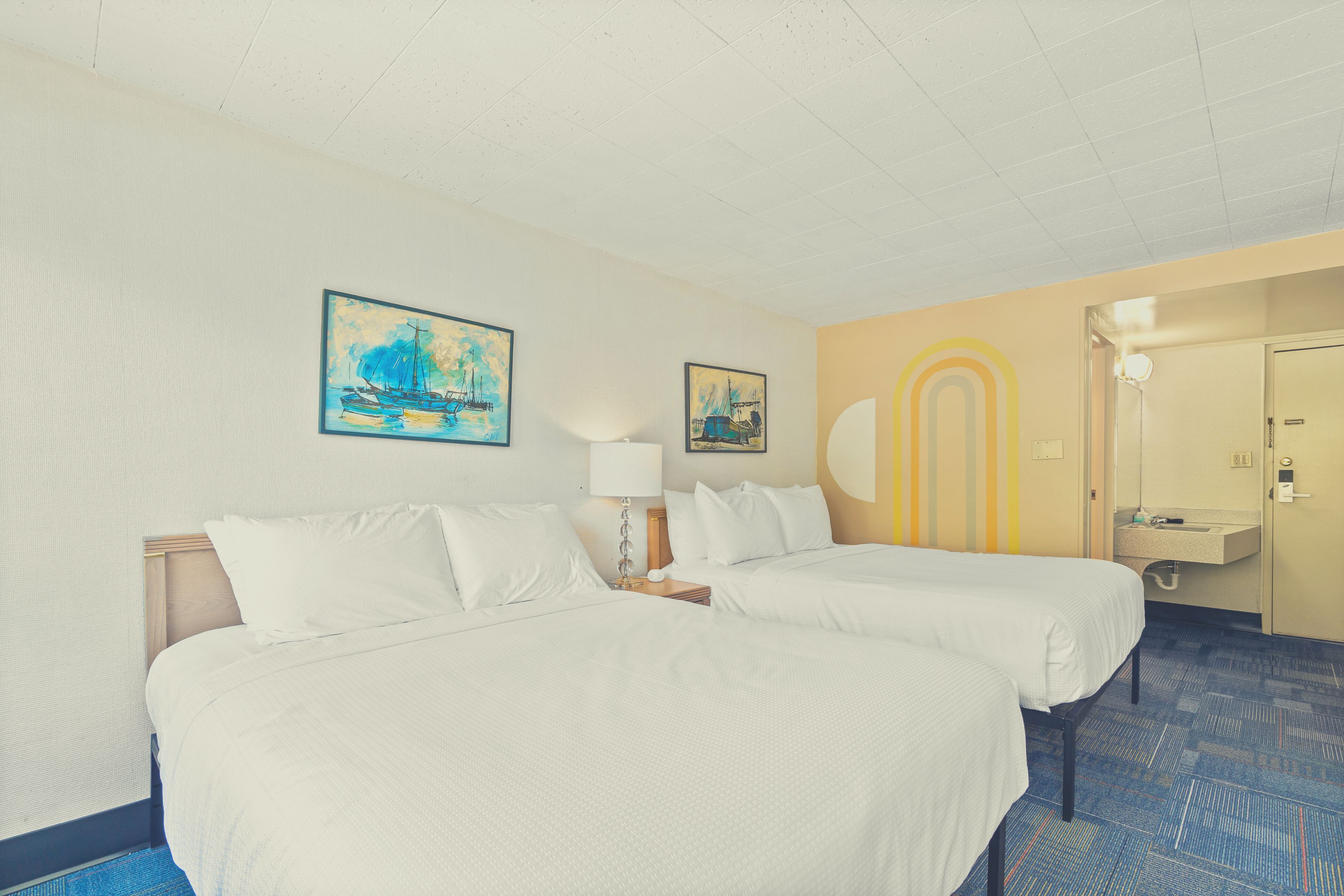 A hotel room with two beds, a bathroom, and artwork on the walls.