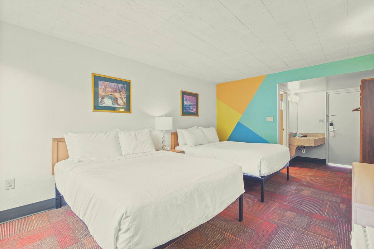 Habitación de hotel con dos camas, un escritorio pequeño, un espejo y la puerta del baño.