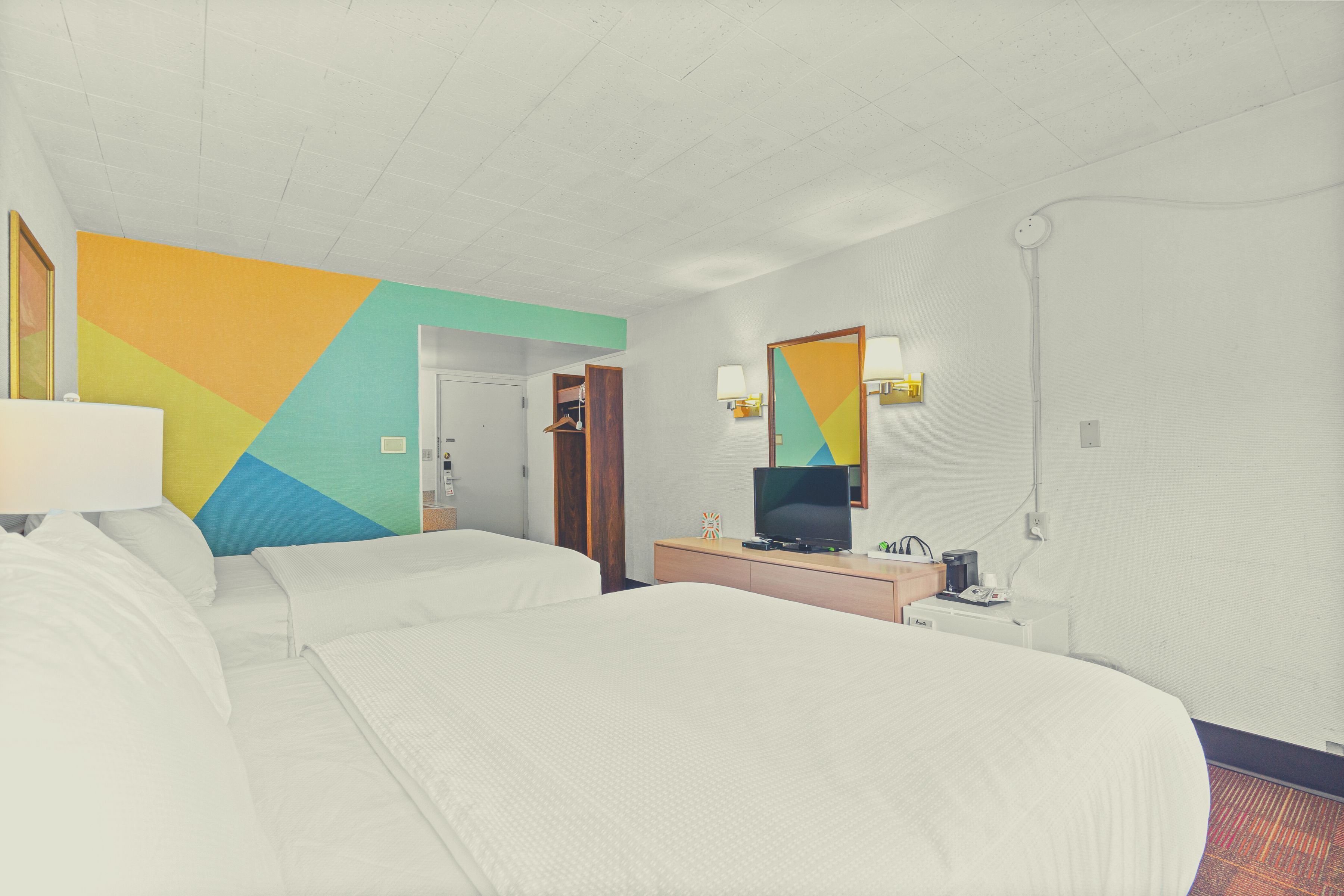 Une chambre d’hôtel avec deux lits, une télévision, un bureau avec une lampe et un mur aux couleurs vives.
