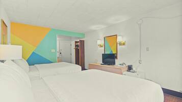 Une chambre d’hôtel avec deux lits, une télévision, un bureau avec une lampe et un mur aux couleurs vives.