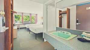 Ett hotellrum med en säng, ett skrivbord, ett fönster med gardiner, ett badrum med handfat och spegel samt en dörr med ett nummer.