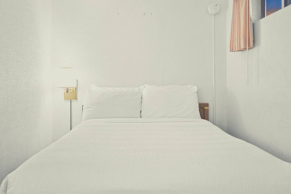 Habitación de hotel minimalista con una cama grande, una mesita de noche y una lámpara fijada a la pared.