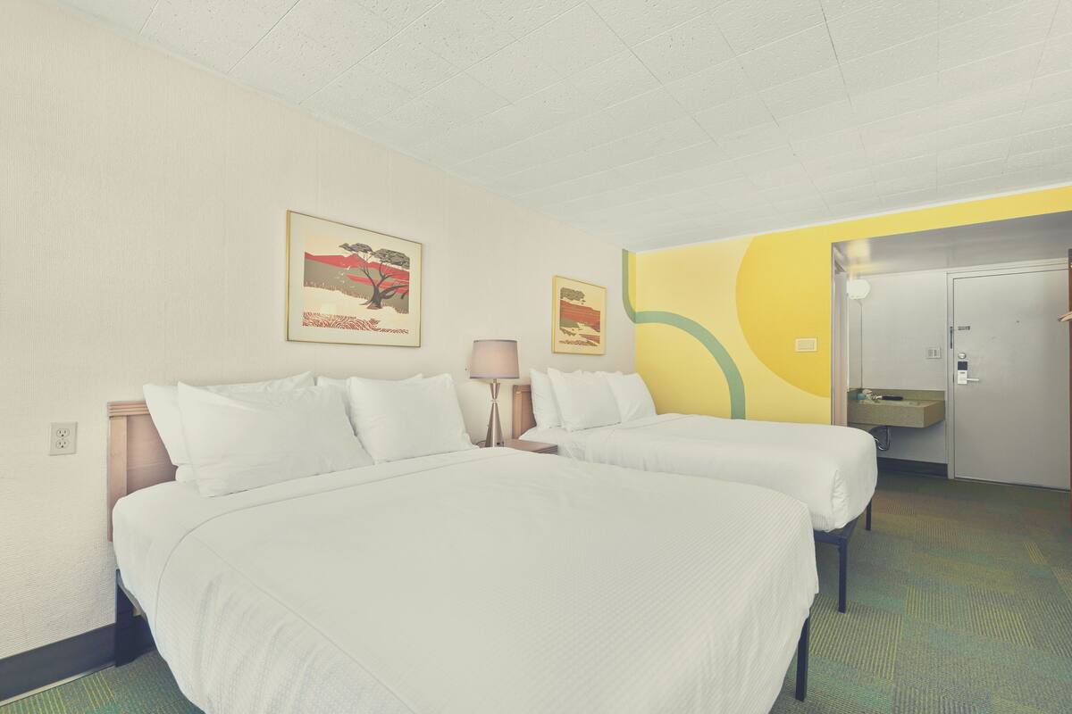 Una habitación de hotel con dos camas, una mesita de noche, una lámpara y obras de arte en las paredes.