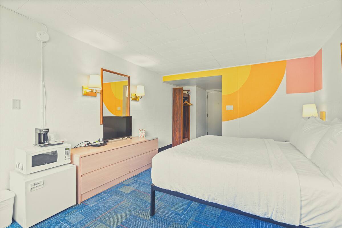 Una habitación de hotel con cama, cómoda, microondas, televisión y espejo.