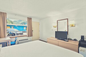 Quarto de hotel com uma cama grande, uma escrivaninha com cadeira, televisão e cómoda.