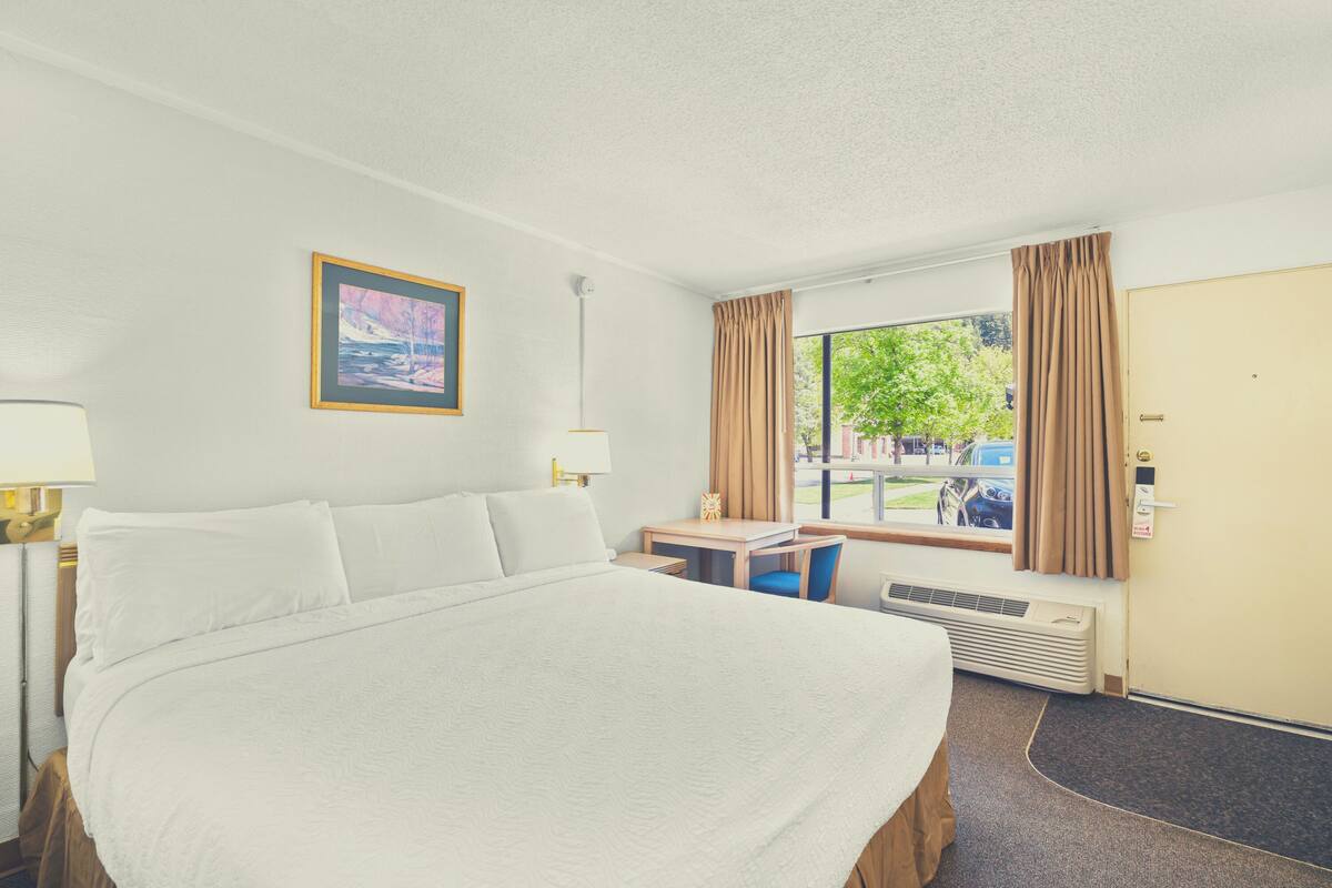Una habitación de hotel con una cama grande, un escritorio, una silla, una ventana con cortinas y una puerta.