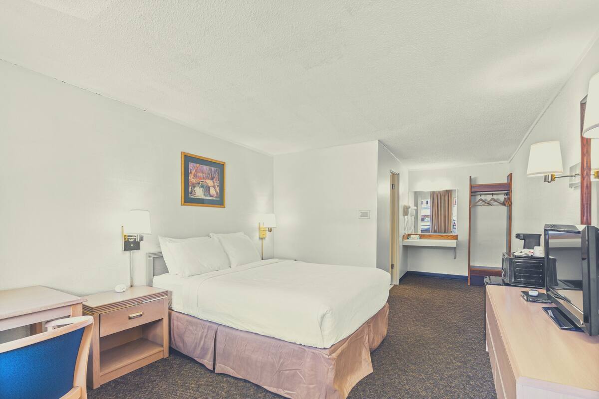 Una habitación de hotel con cama, mesita de noche, lámpara, escritorio, silla y televisor.