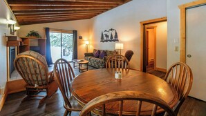 A dining area with a wooden table and chairs, a sofa, and a wall-mounted lamp. - Timbers at Island Park Village Resort (Island Park)