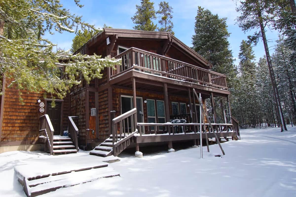 Une cabane en bois dotée d’un balcon et d’un escalier menant à l’entrée, entourée de neige et d’arbres.